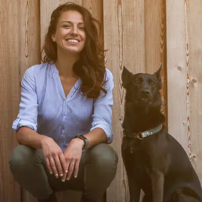 Franziska Koch mit ihrem schwarzen Hund vor einer Holzwand